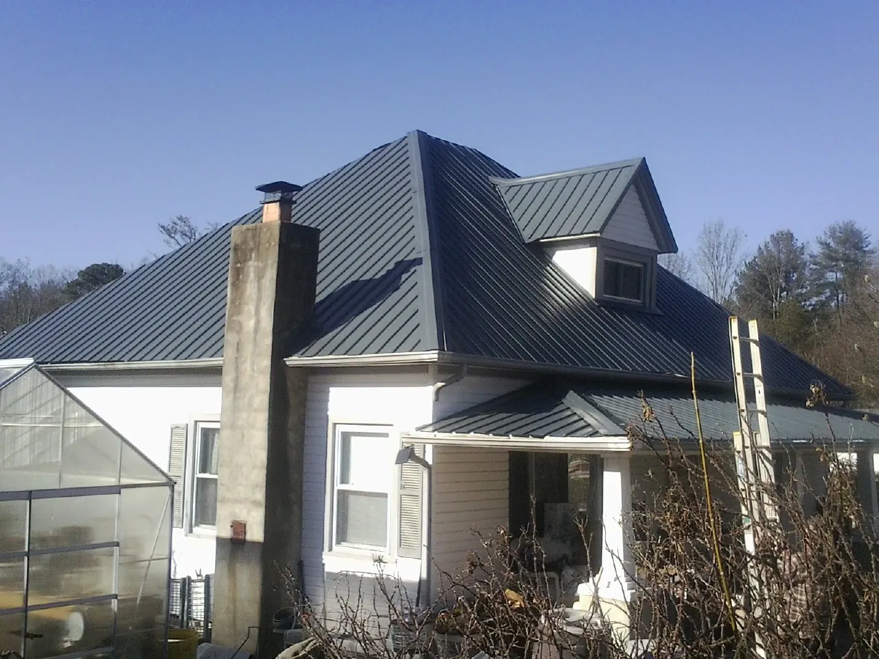 Dark blue standing seam metal roof on a white farmhouse with dormer — Slate & Tile Roof Repair by Roofing Brothers in Hinesville