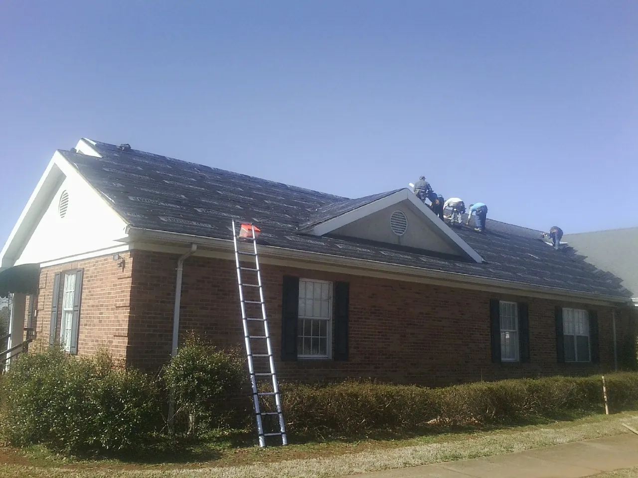 Crew tearing shingles off a brick ranch roof with a ladder set — Emergency Roof Repair work by our crew in Hinesville