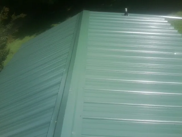 New green metal panels meeting at the ridge of a roof — Flat Roof Repair work by our crew in Hinesville