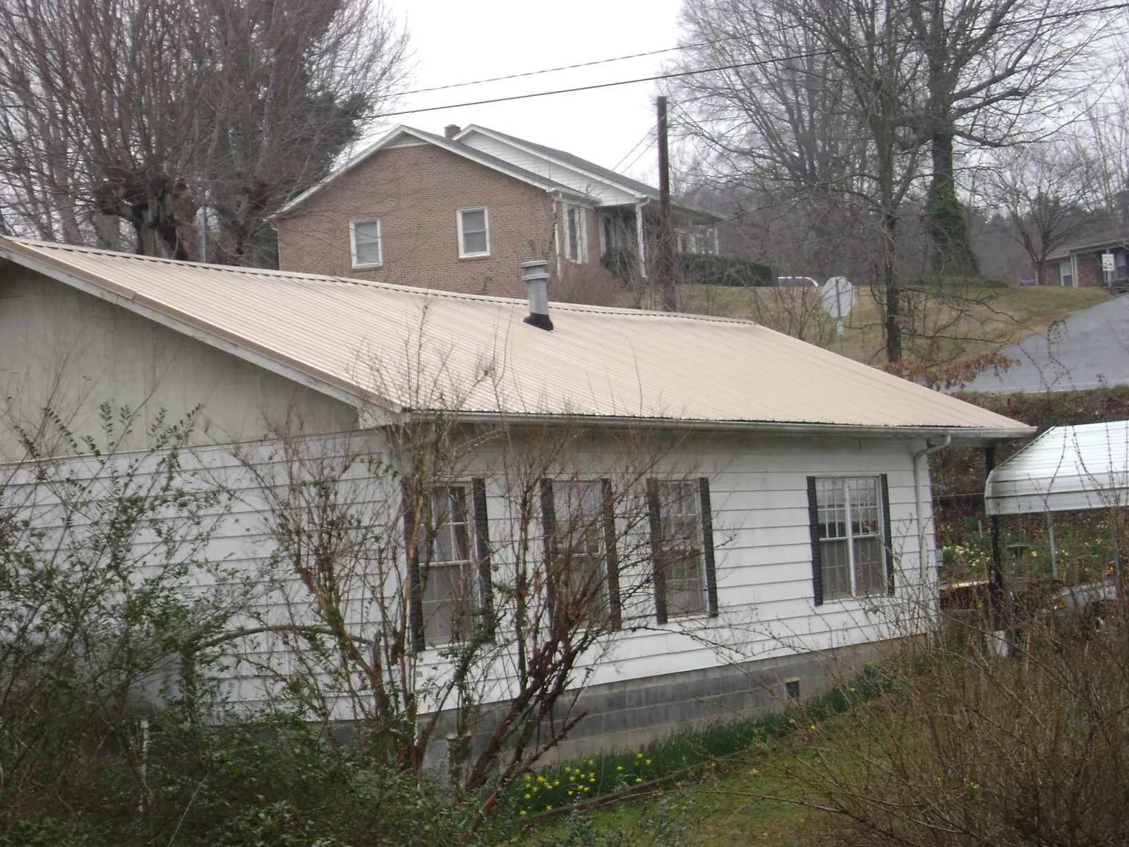 Tan metal roof on a white sided house set into a hillside — Commercial Roofing by Roofing Brothers in Hinesville