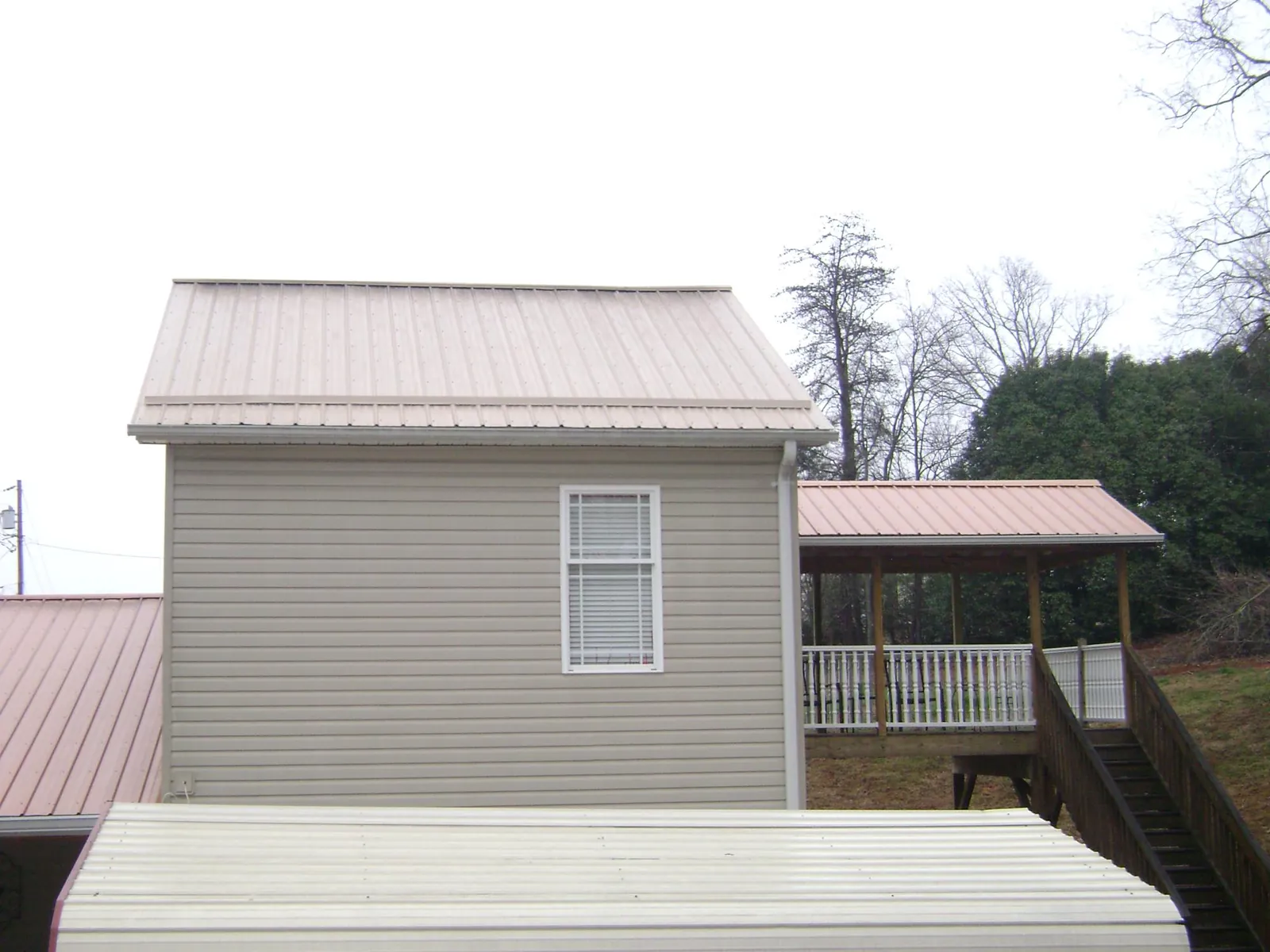 Tan metal roofs on a two story addition and attached porch, from a Roof Replacement job in Hinesville